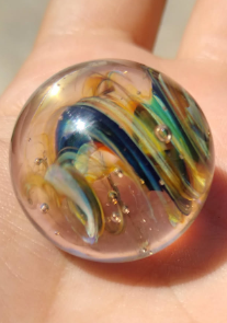 A marble mostly clear with wispy swirls of blue and green.